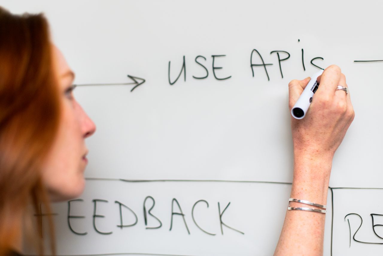 Mastering the First Impression: Your intriguing post title goes here A woman writes 'Use APIs' on a whiteboard, focusing on software planning and strategy.